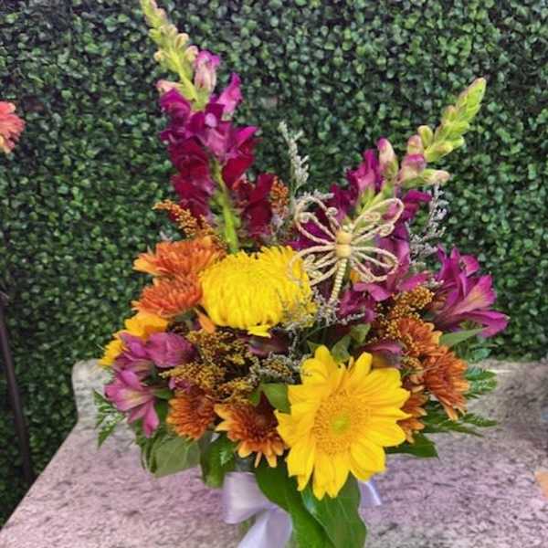 Colorful bouquet of yellow and orange flowers in a glass vase with a ribbon
