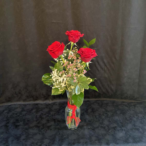 Three red roses in a clear glass vase with a red ribbon