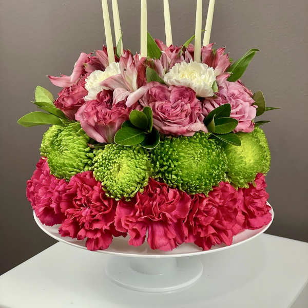 Pink and green floral centerpiece with white candles on a pedestal stand