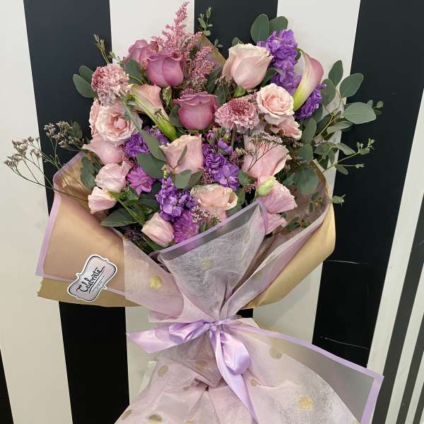 Bouquet of pink and purple flowers wrapped in pastel paper with a ribbon