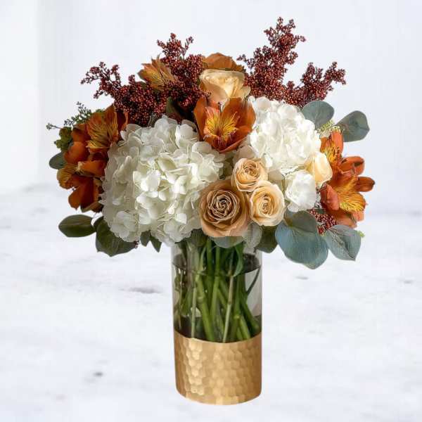 Bouquet of white hydrangeas, peach roses, and orange flowers in a glass vase