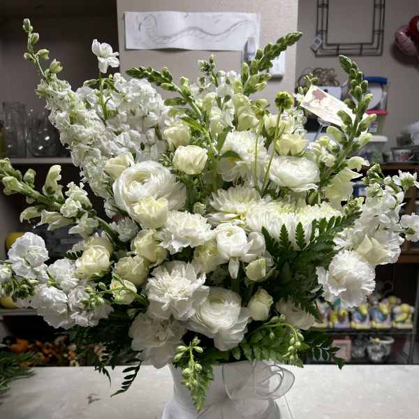 White floral arrangement in a white vase with a sheer ribbon