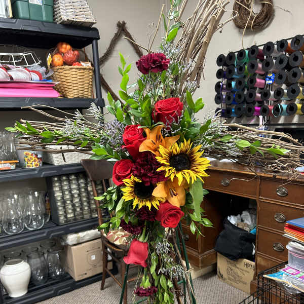 Tall floral cross with red roses, sunflowers, and orange lilies