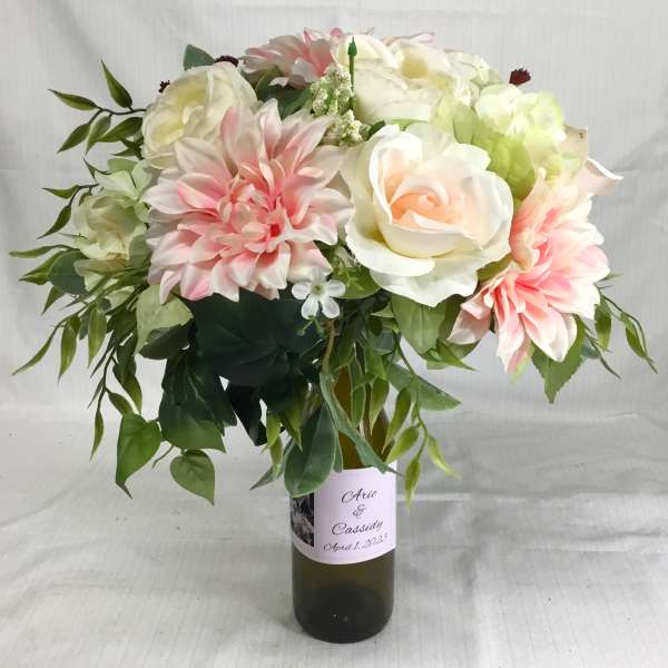 Silk wedding arrangement of white and blush flowers in a green glass bottle with custom label