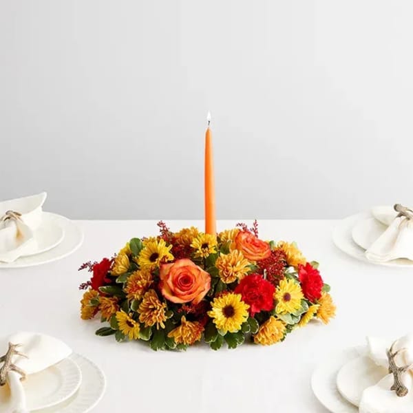Low floral centerpiece with an orange taper candle