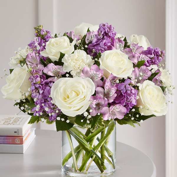 White roses and purple flowers arranged in a clear glass vase