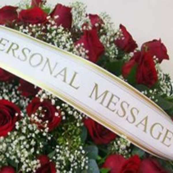 Spray of red roses and white filler flowers with a personalized message banner across the front