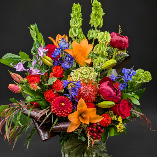 Colorful mixed bouquet in a clear glass vase with lilies, roses, and peonies