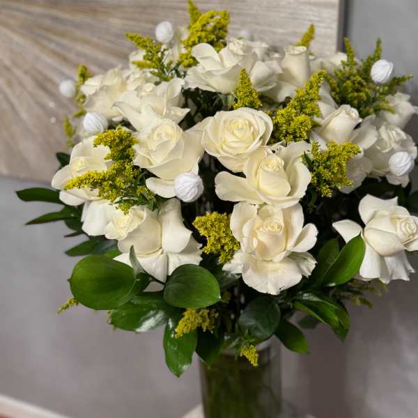 White roses arranged in a glass vase with yellow filler flowers