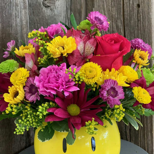 Bright mixed bouquet in a yellow smiley-face vase