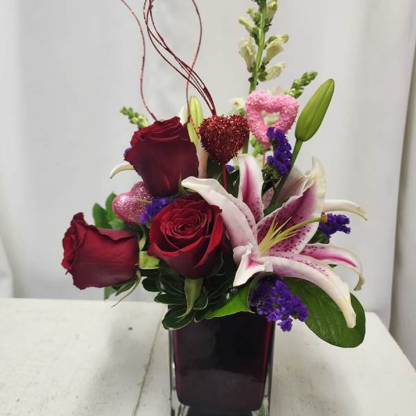 Red roses and pink lilies in a square glass vase with heart picks