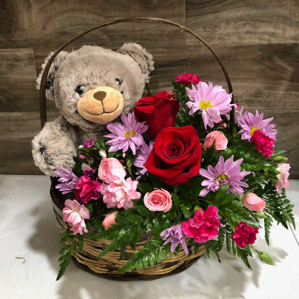 Teddy bear in a basket with red roses and pink flowers