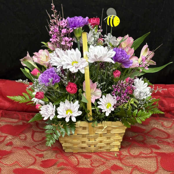 Basket arrangement of white daisies, pink and purple flowers, and a bee pick