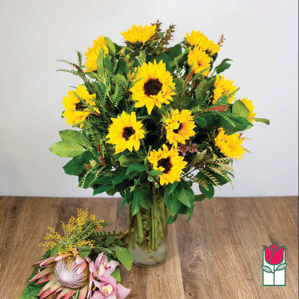 Sunflower bouquet in a clear glass vase with a small pink tropical flower cluster beside it