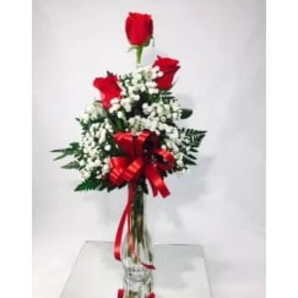 Red roses arranged with white baby's breath in a clear vase with a red ribbon