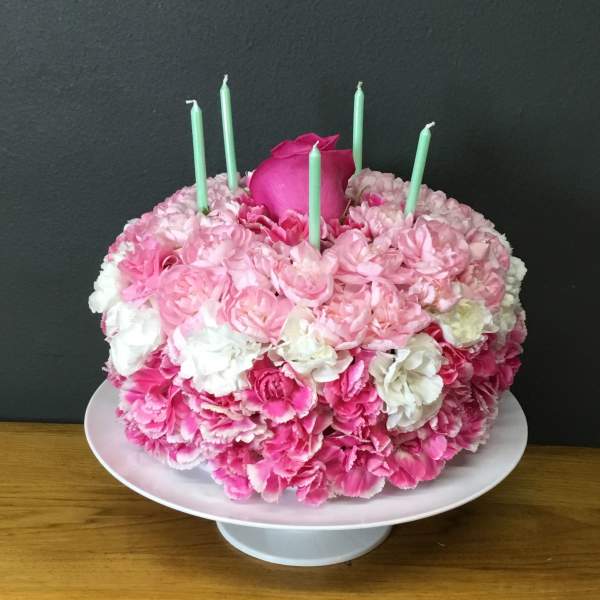 Pink and white floral cake with mint green candles on a pedestal stand