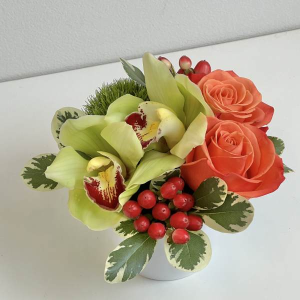 Compact bouquet with orange roses, green orchids, and red berries in a white vase