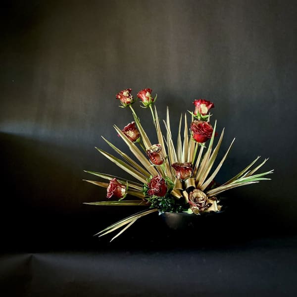 Red roses arranged with spiky dried foliage in a dark vase