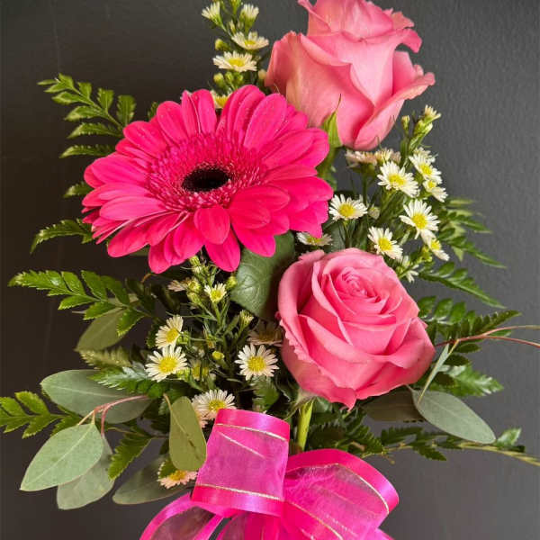 Pink roses and a hot pink gerbera daisy in a glass vase with a ribbon