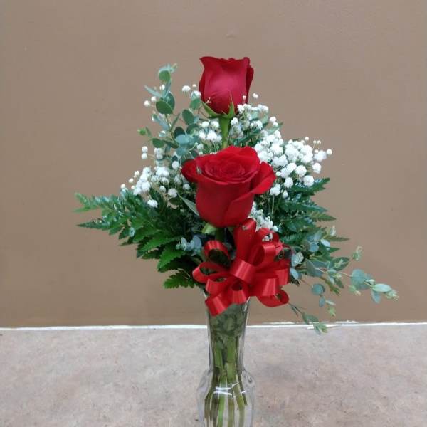 Two red roses in a clear glass vase with baby's breath and a red ribbon