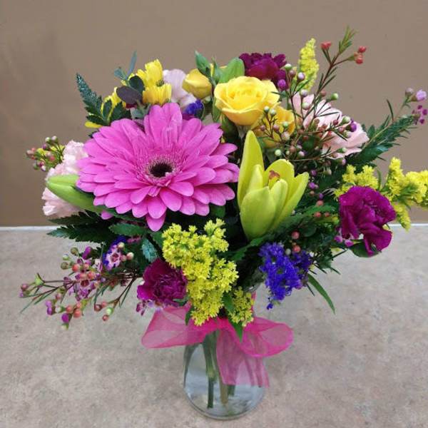 Colorful mixed bouquet in a clear glass vase with a pink ribbon