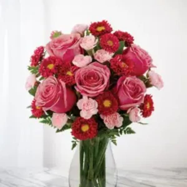 Pink roses and red daisy-like flowers arranged in a clear glass vase