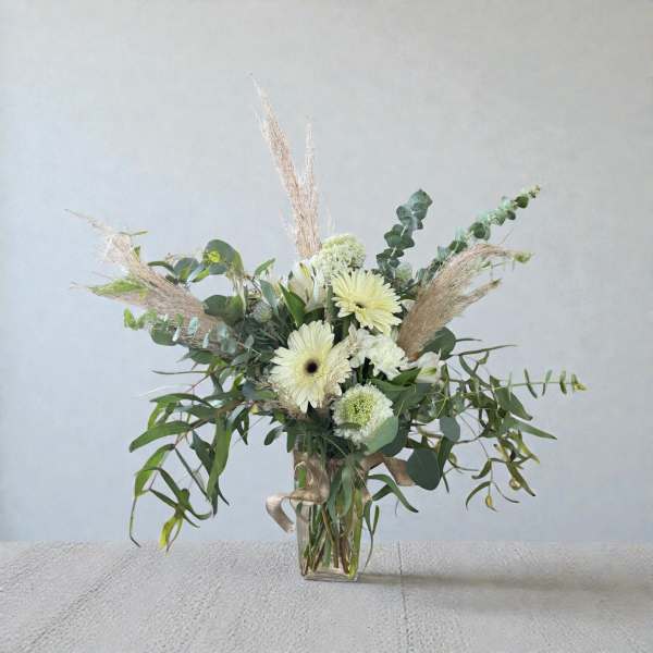 White gerbera daisies and greenery in a clear glass vase