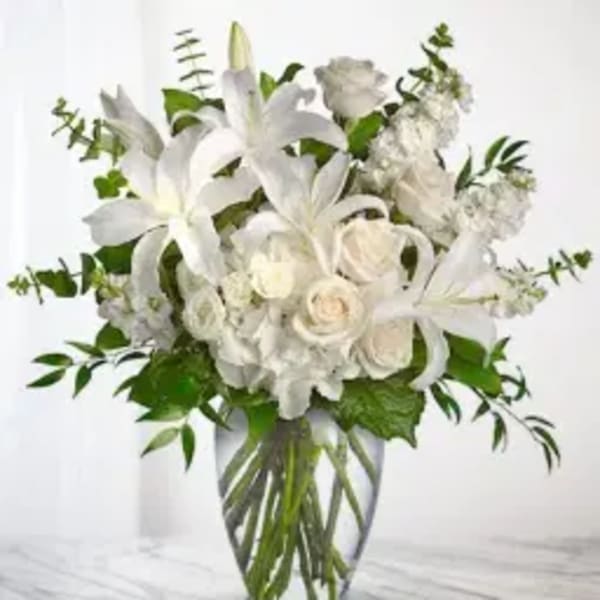 White lilies and roses in a clear glass vase with greenery