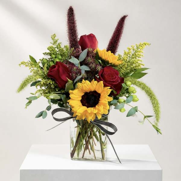 Bouquet of red roses and sunflowers in a glass vase with a striped ribbon