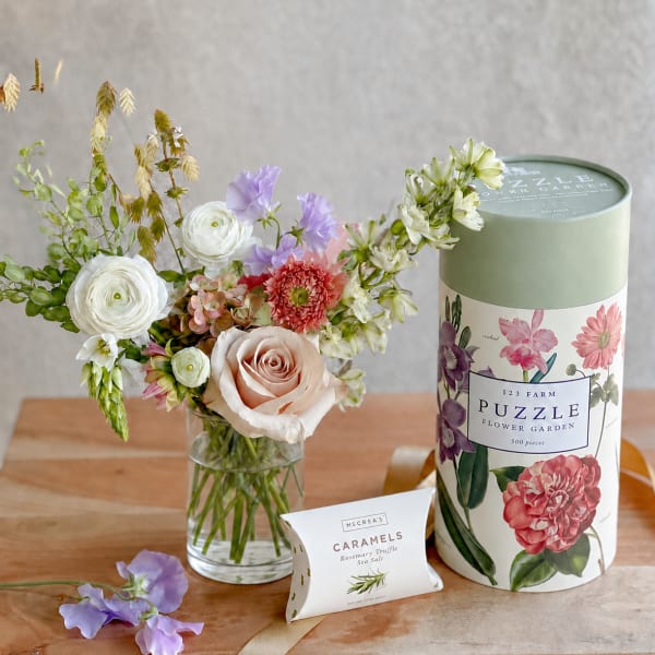 Flower arrangement in a glass vase beside a puzzle tin and caramel box