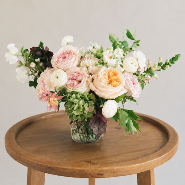 Mixed pastel flower arrangement in a glass vase on a wooden table