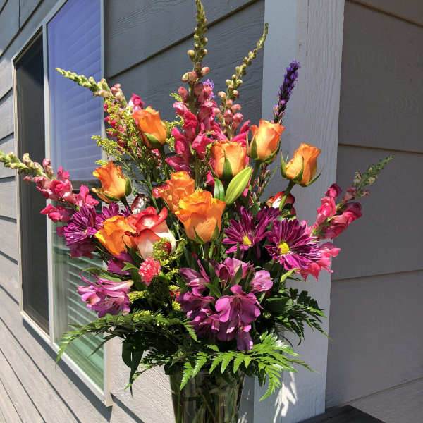 Tall bouquet of orange roses, pink snapdragons, and purple daisies in a glass vase