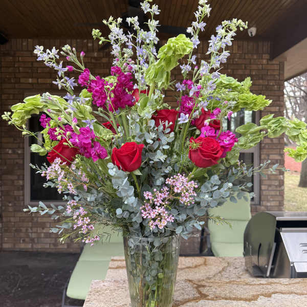 Tall bouquet of red roses and pink flowers in a clear glass vase