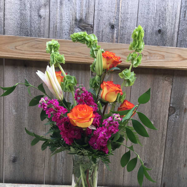 Orange and yellow roses in a clear glass vase with magenta flowers