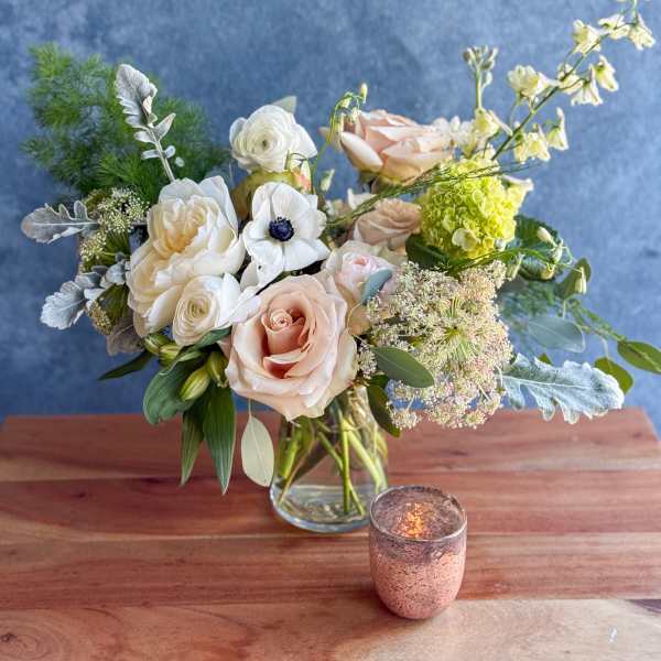 Blush and white bouquet in a clear glass vase with a small candle nearby