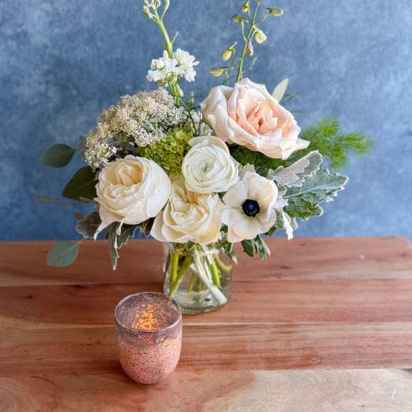 Cream and blush flowers arranged in a clear glass vase with a candle in front.