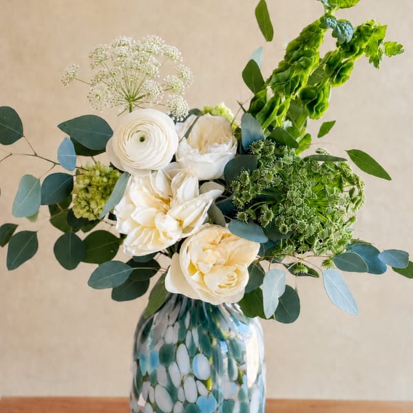White flowers in a patterned glass vase with blue-green foliage