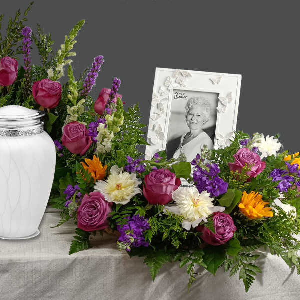 Funeral urn surrounded by purple, white, and orange flowers with a framed portrait
