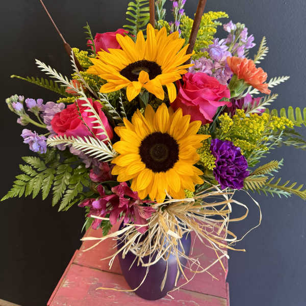Bouquet of sunflowers, pink roses, and purple flowers in a vase