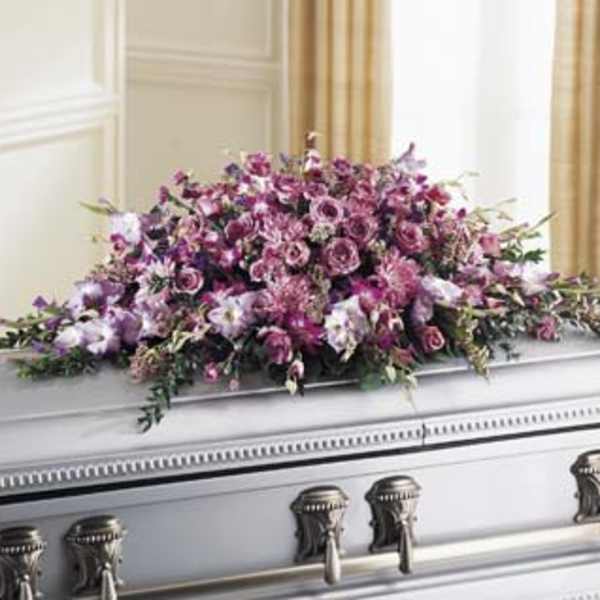 Lavender and pink mixed-flower casket spray in a long cascading design on a silver casket.