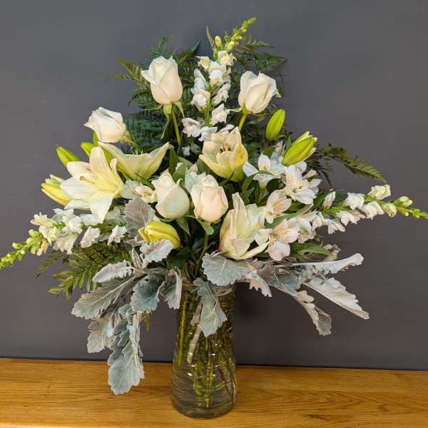 White lilies and roses arranged in a glass vase with silver foliage