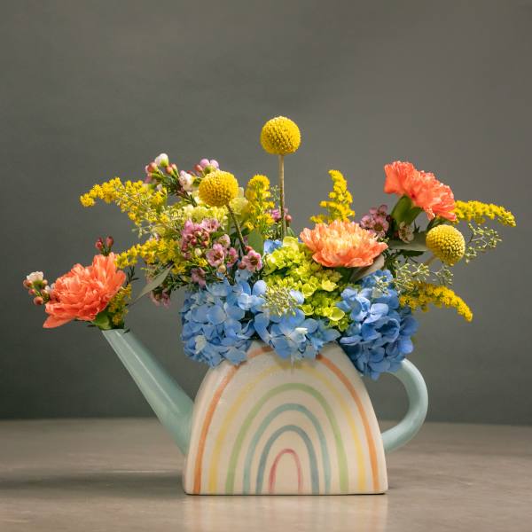 Colorful flowers arranged in a pastel watering can vase with a rainbow design