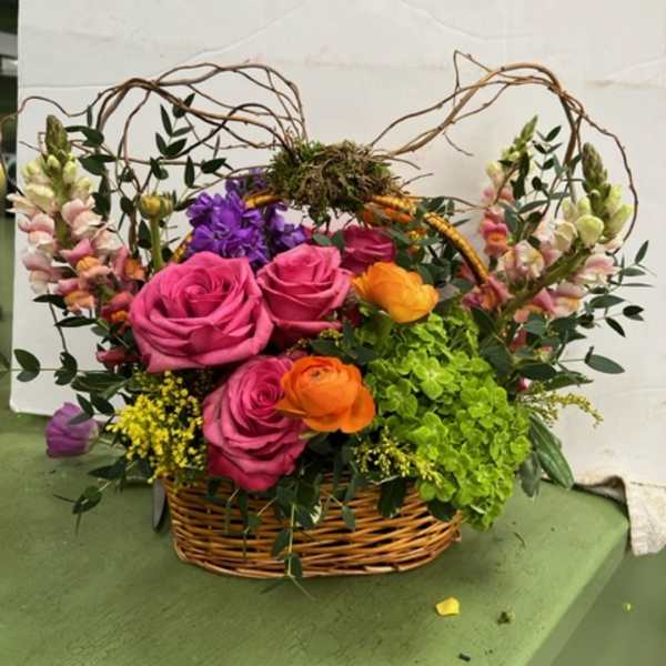 Basket arrangement with pink roses, orange ranunculus, and purple blooms