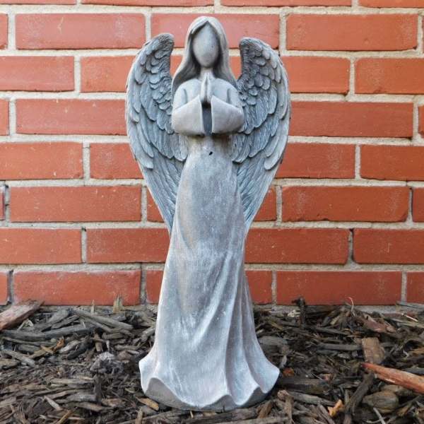 Gray angel statue with folded hands against a brick wall