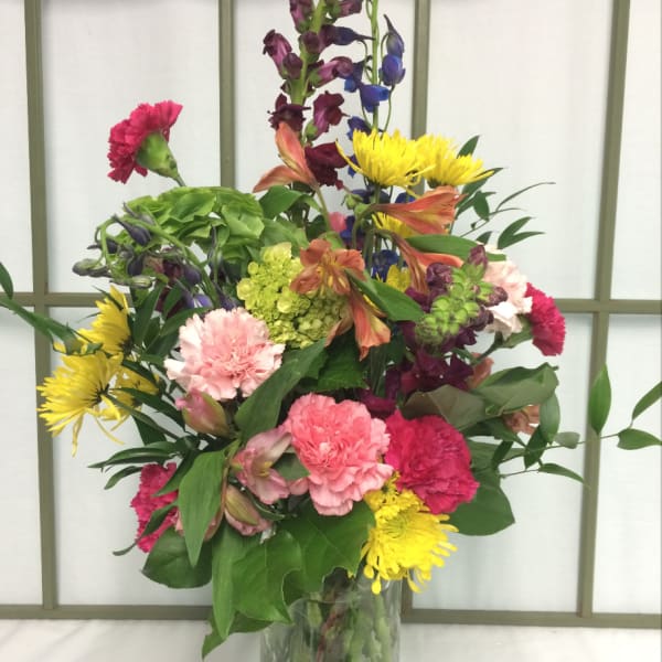 Colorful mixed bouquet in a clear glass vase with pink, yellow, purple, and orange blooms