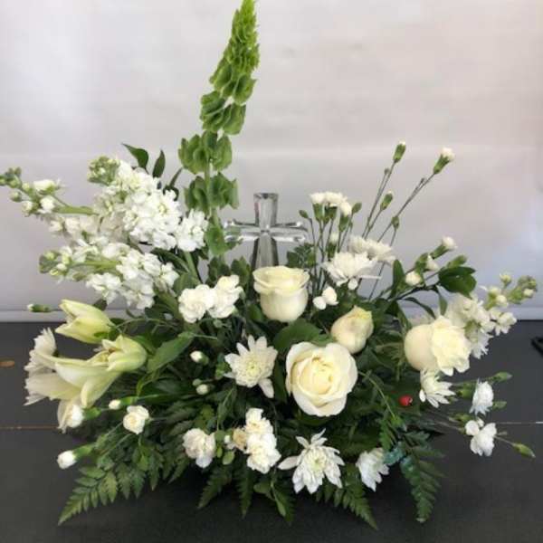 White floral arrangement with roses, lilies, and daisies around a silver cross