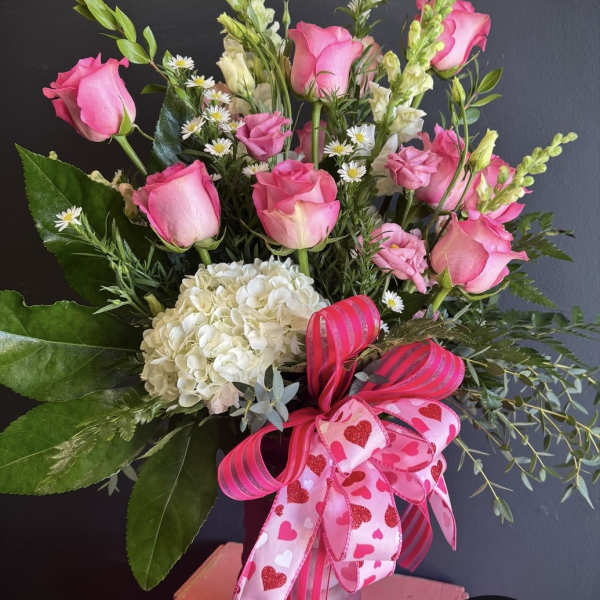 Pink roses and white hydrangea in a glass vase with heart ribbons