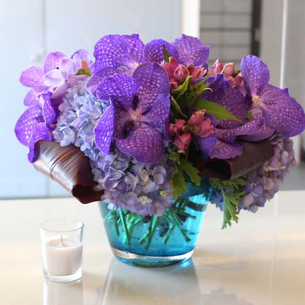 Purple orchid and hydrangea arrangement in a blue glass vase