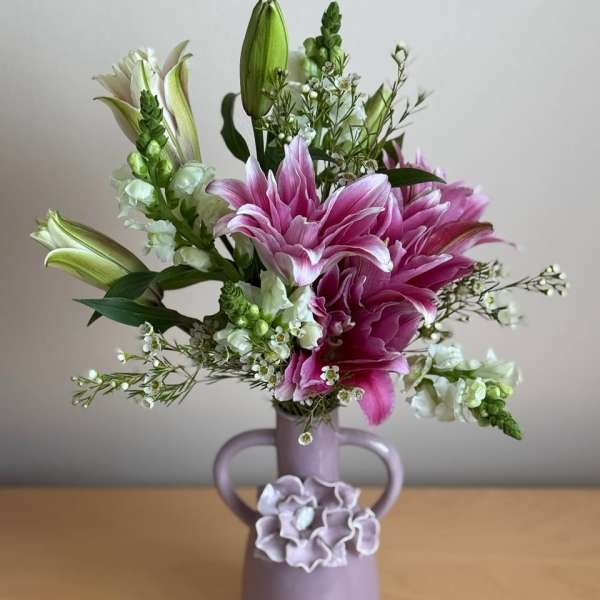 Pink lilies and white flowers in a lavender vase