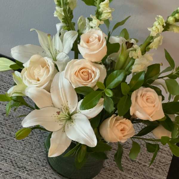 Cream roses and white lilies arranged in a dark vase